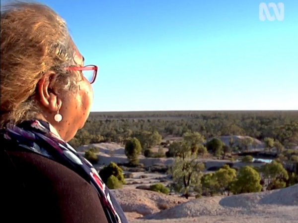 Screengrab from television with woman in foreground looking out over outback.