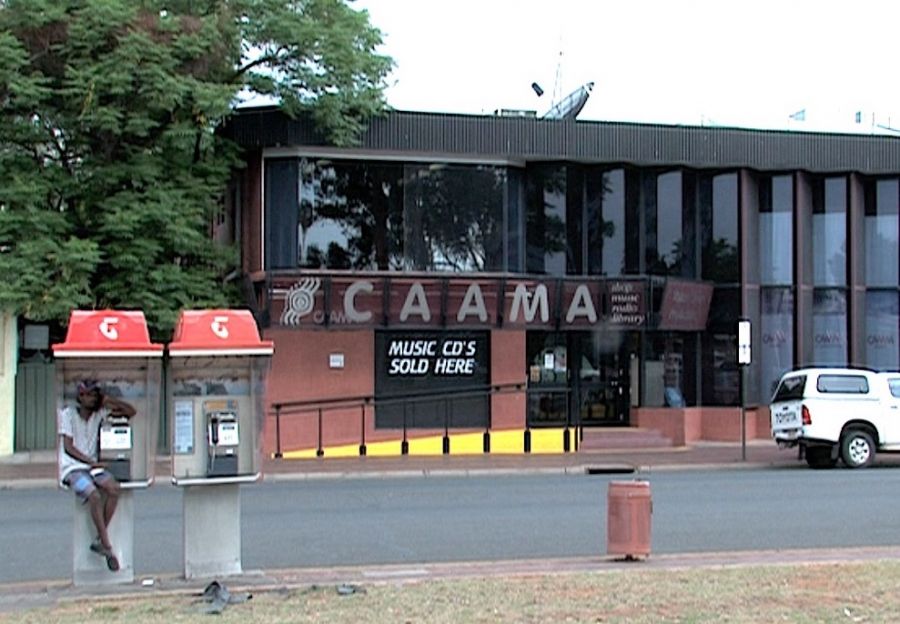 Photograph of building, CAAMA. In the foreground a man sits in a phonebooth..