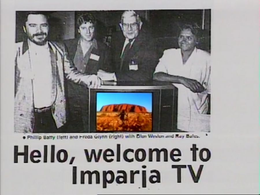 News article screengrab featuring three men and one woman leaning on a colour TV. Caption states Hello, Welcome to Imparja TV...